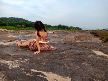 Side view of woman sitting on land against sky