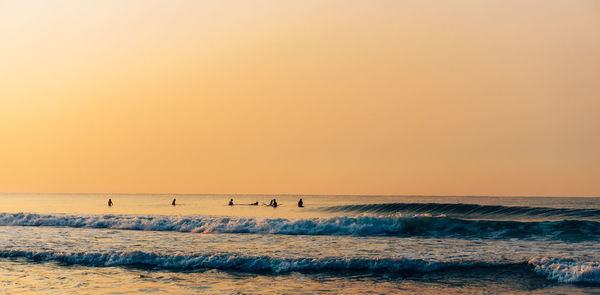 Scenic view of sea against clear sky during sunrise and surfers surfing