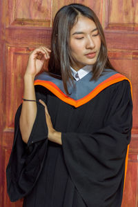 Thoughtful young woman in graduation gown standing door