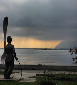 Charlie chaplin statue in vevey with a fork sculpture against the lake with a storm in background