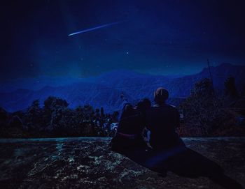 Rear view of couple sitting against sky at night