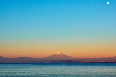 Scenic view of sea snowcapped mountain against clear sky during sunrise