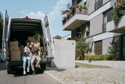 Multiracial couple sitting in van trunk near building
