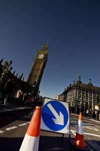 Tilt image of arrow symbol with traffic cones on city street by big ben against clear blue sky