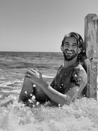 Portrait of smiling shirtless man sitting in sea