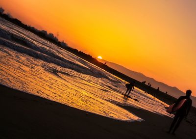 Silhouette people on beach against orange sky