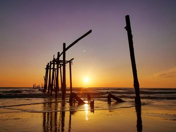 Silhouette wooden posts on beach against sky during sunset