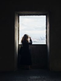 Rear view of mid adult woman standing by window in building