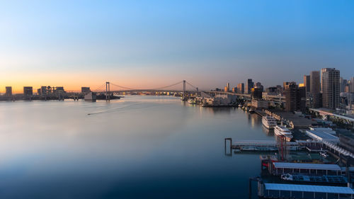 Bridge over river by city buildings against sky