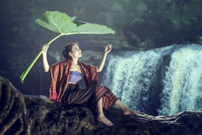 Young woman sitting on rock against waterfall