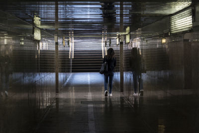 Rear view of woman walking on illuminated walkway at night