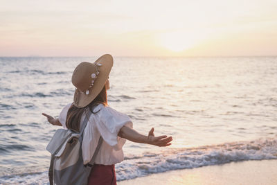 Woman standing on beach against sky during sunset