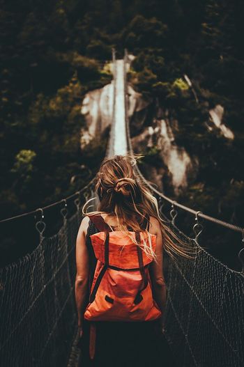 Rear view of woman standing on footbridge at forest