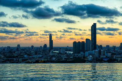 Sea by buildings against sky during sunset