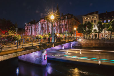 Illuminated buildings by river in city at night