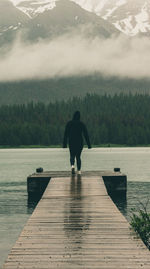 Rear view of man standing on pier over lake
