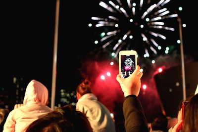 Cropped hand of woman photographing firework display with smart phone at night
