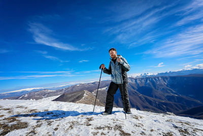 Rear view of man standing on snowcapped mountain against sky