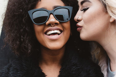 Portrait of woman in sunglasses and fur coat with friend against wall