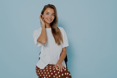 Portrait of young woman standing against blue background