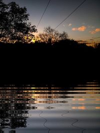 Silhouette trees by lake against sky during sunset