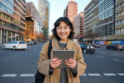 Portrait of young woman using mobile phone in city