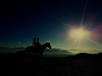 Silhouette person on horse on field against sky during sunset