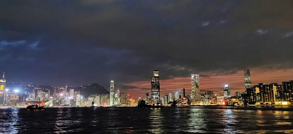 Illuminated buildings by river against sky at night