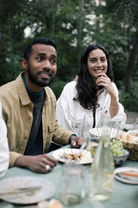 Smiling woman with hand on chin sitting by male friend at dinner party
