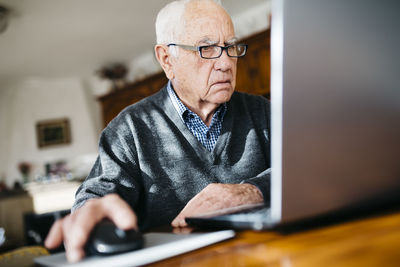 Portrait of serious looking senior man using laptop at home