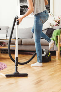 Low section of teenage girl using vacuum cleaner in living room