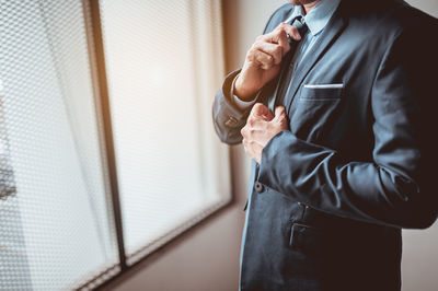 Midsection of man holding hands while standing by window