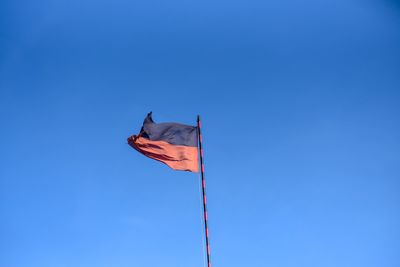 Low angle view of flag waving against clear blue sky