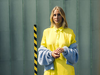 Young woman standing against yellow wall