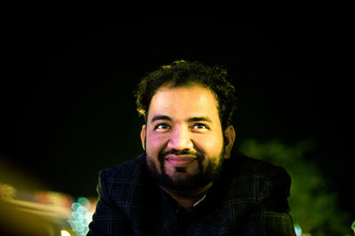 Close-up of thoughtful young man smiling against sky at night