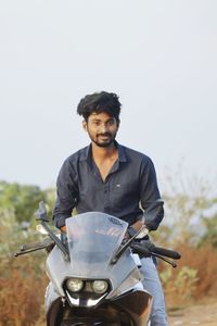 Portrait of young man riding motorcycle against sky