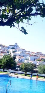 People by swimming pool in city against clear sky