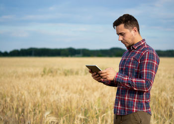 Young man using mobile phone while standing on field