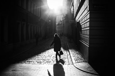 Silhouette woman walking on street amidst buildings