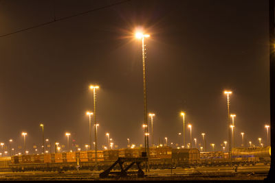 Illuminated factory by street against sky at night