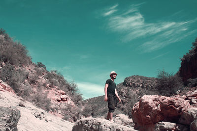 Young man standing on rock against sky