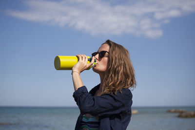 Portrait of young woman drinking water from sea against sky
