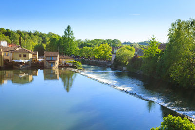 Scenic view of river by trees and houses against sky