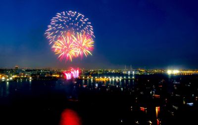 Firework display over illuminated city against sky at night