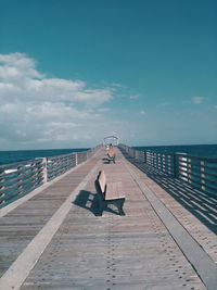 Man sitting on pier over sea against sky