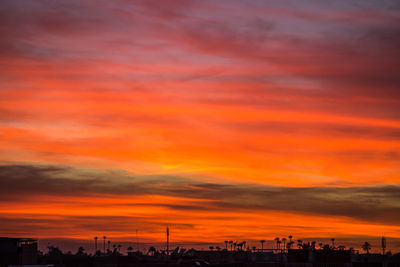 Silhouette of city against cloudy sky during sunset