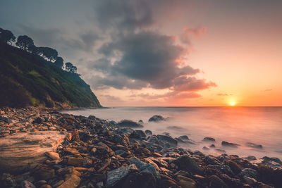 Scenic view of sunset at rocky shore by sea against sky
