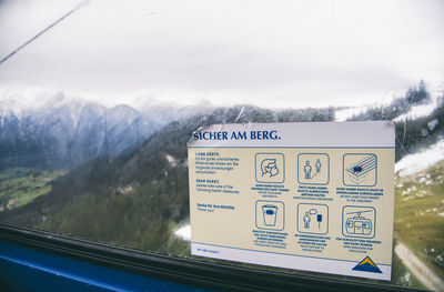 Information sign on snowcapped mountains seen through window
