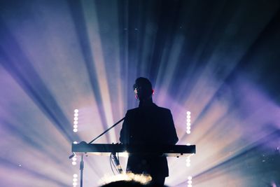 Rear view of silhouette man standing at music concert