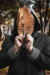 Man covering face with leaf during autumn